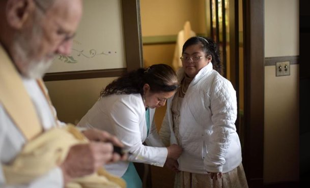 Father Patrick Dolan fiddles with audio equipment as Irma Bahena zips up the coat of her daughter, Jennifer Bahena. Fr. Dolan, an Irish native, offered this Mass in Spanish.